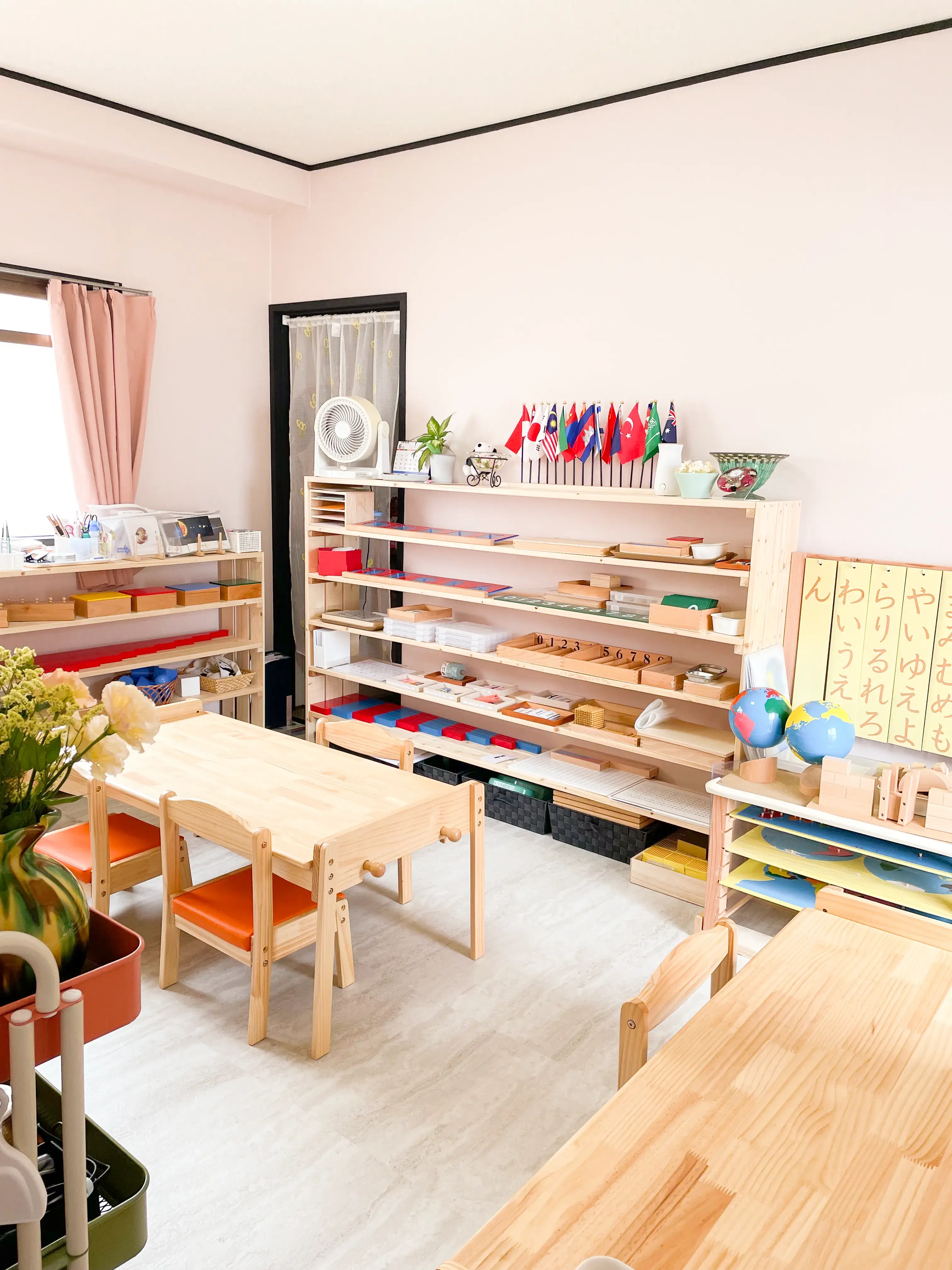 モンテッソーリ教具が並ぶ棚と木製の机がある保育室